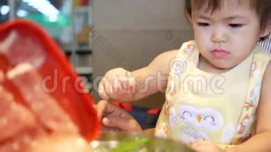 一个亚洲小女孩帮她妈妈把烹饪材料放进<strong>沸腾</strong>的<strong>火锅</strong>里